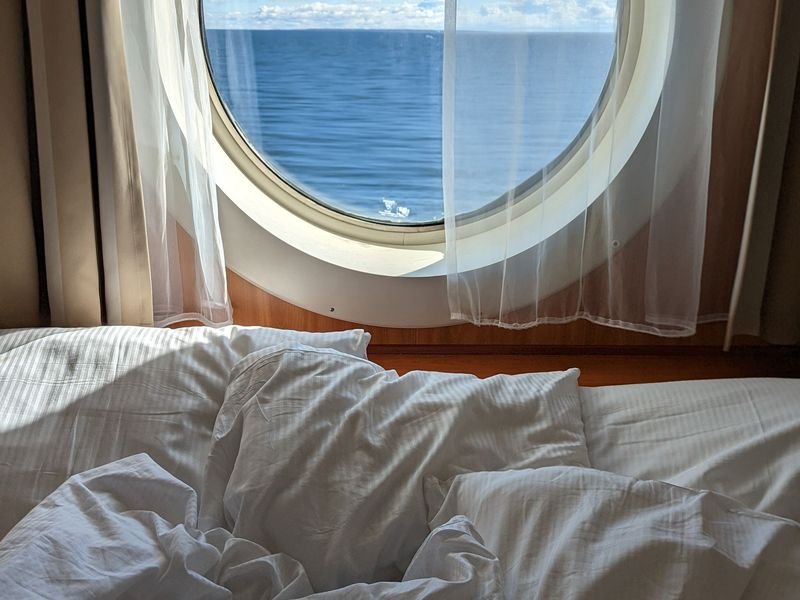 A cabin bed beside a porthole looking out to sea