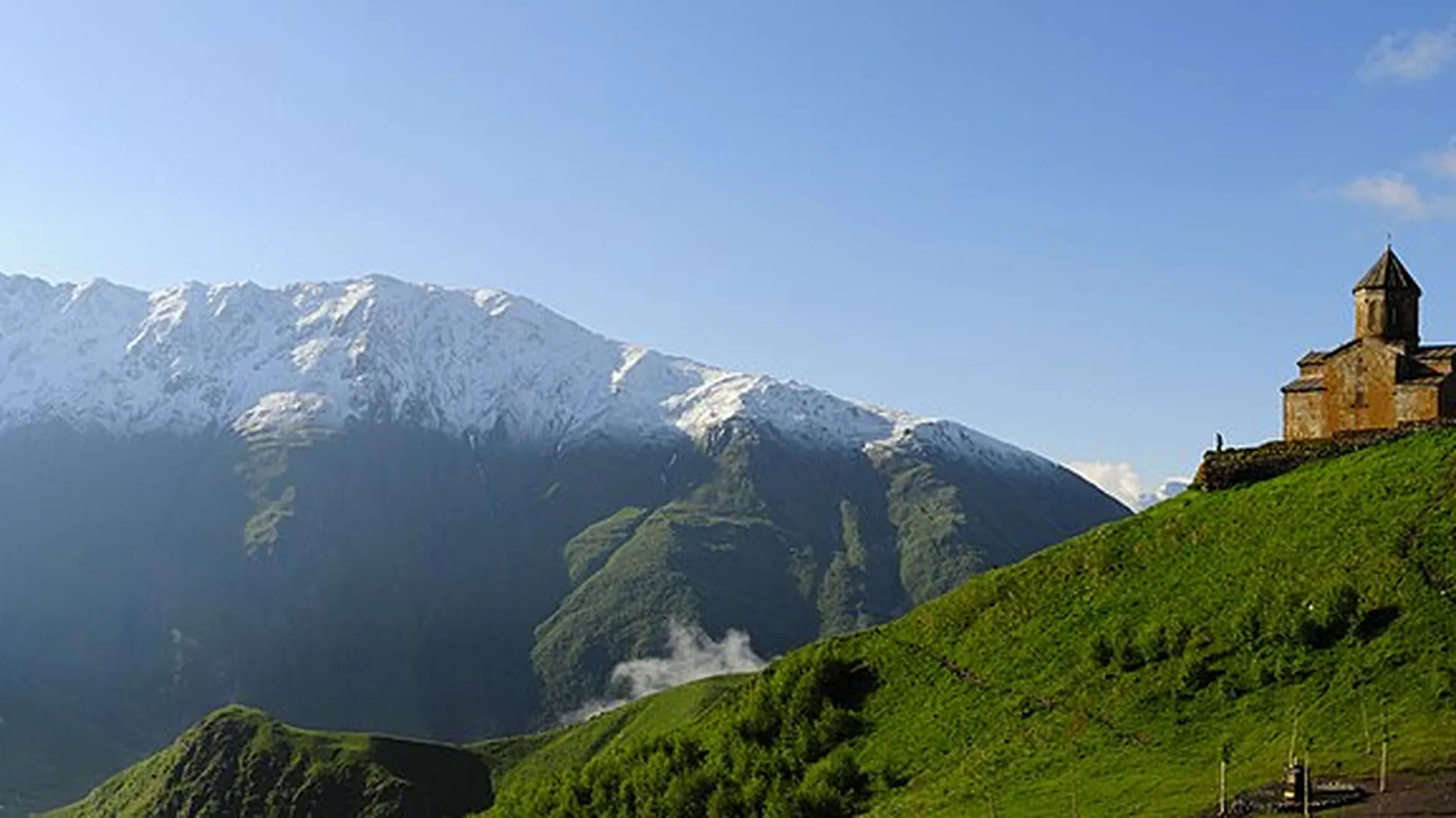 Gergeti Trinity Church on its green ridge beneath the snow-capped peaks of the Caucasus near Kazbegi