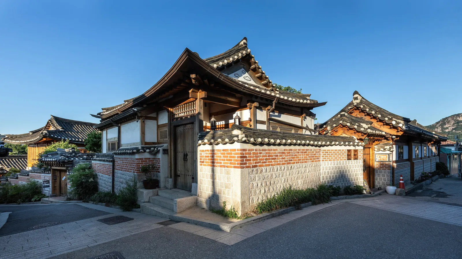 Traditional hanok houses with tiled roofs glow in the golden hour light of Bukchon Hanok Village in Seoul