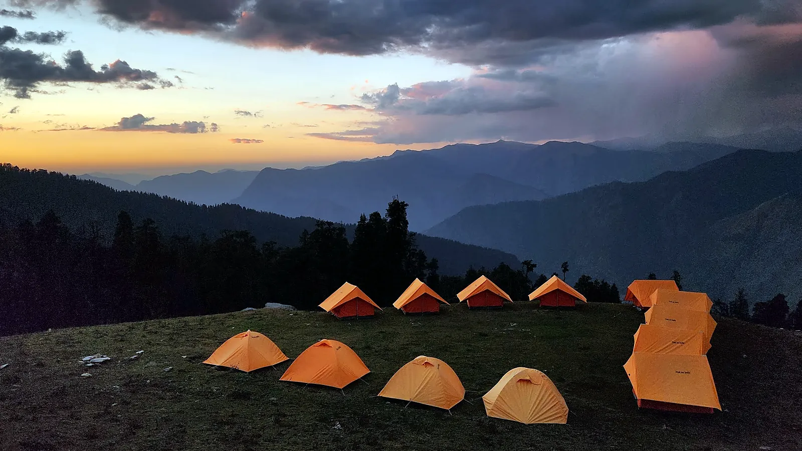 Tents pitched in the snow at a Kedarkantha campsite, with the high peaks of the Garhwal Himalaya on the horizon