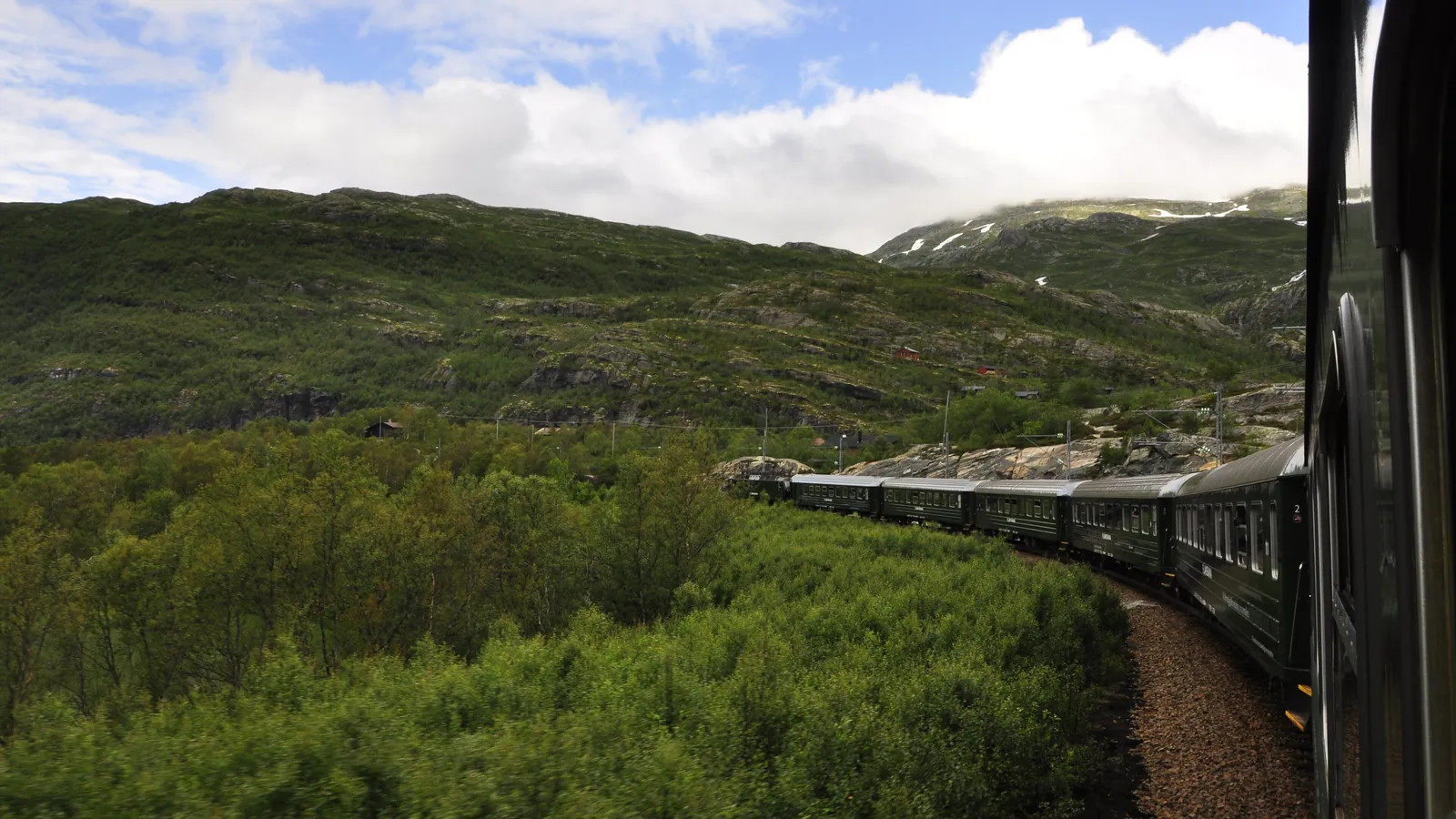 A Flam Railway train winds through green mountain valleys on its steep descent to the fjord