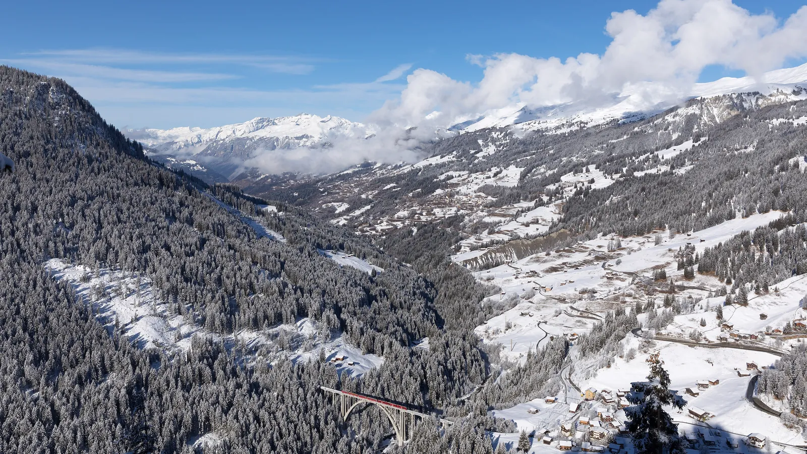 A Swiss train passes through a mountain village in the Alps