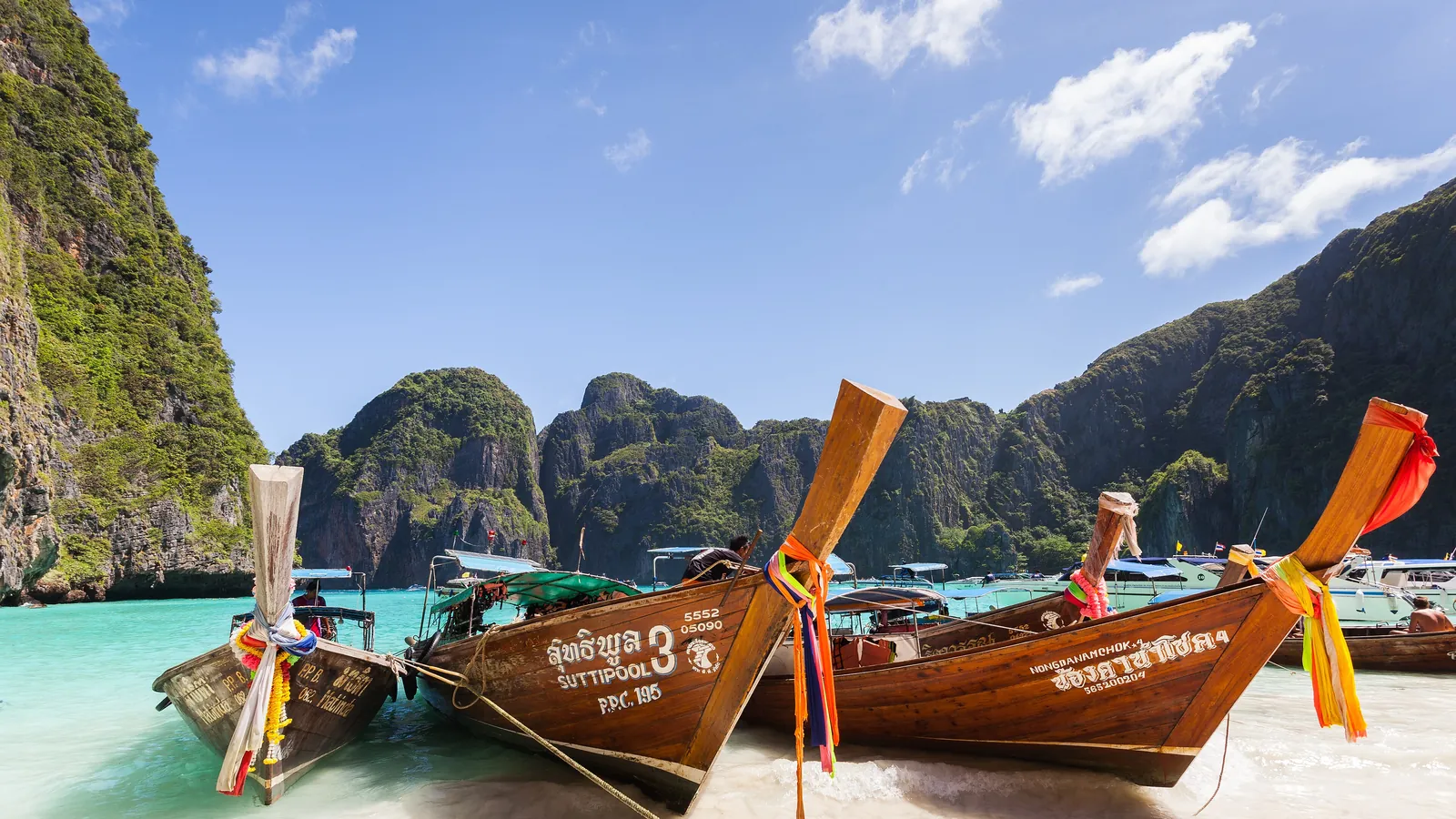 Long-tail boats moored at Maya Bay on Phi Phi Leh, framed by towering limestone cliffs