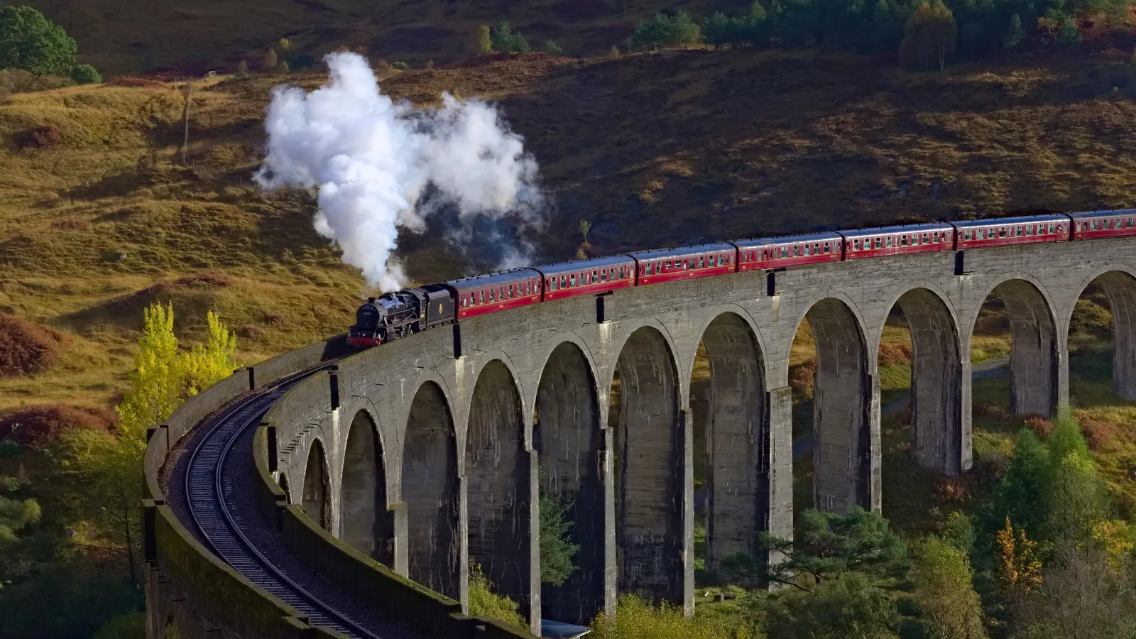 The Jacobite steam train crosses the curving arches of the Glenfinnan Viaduct in the Scottish Highlands