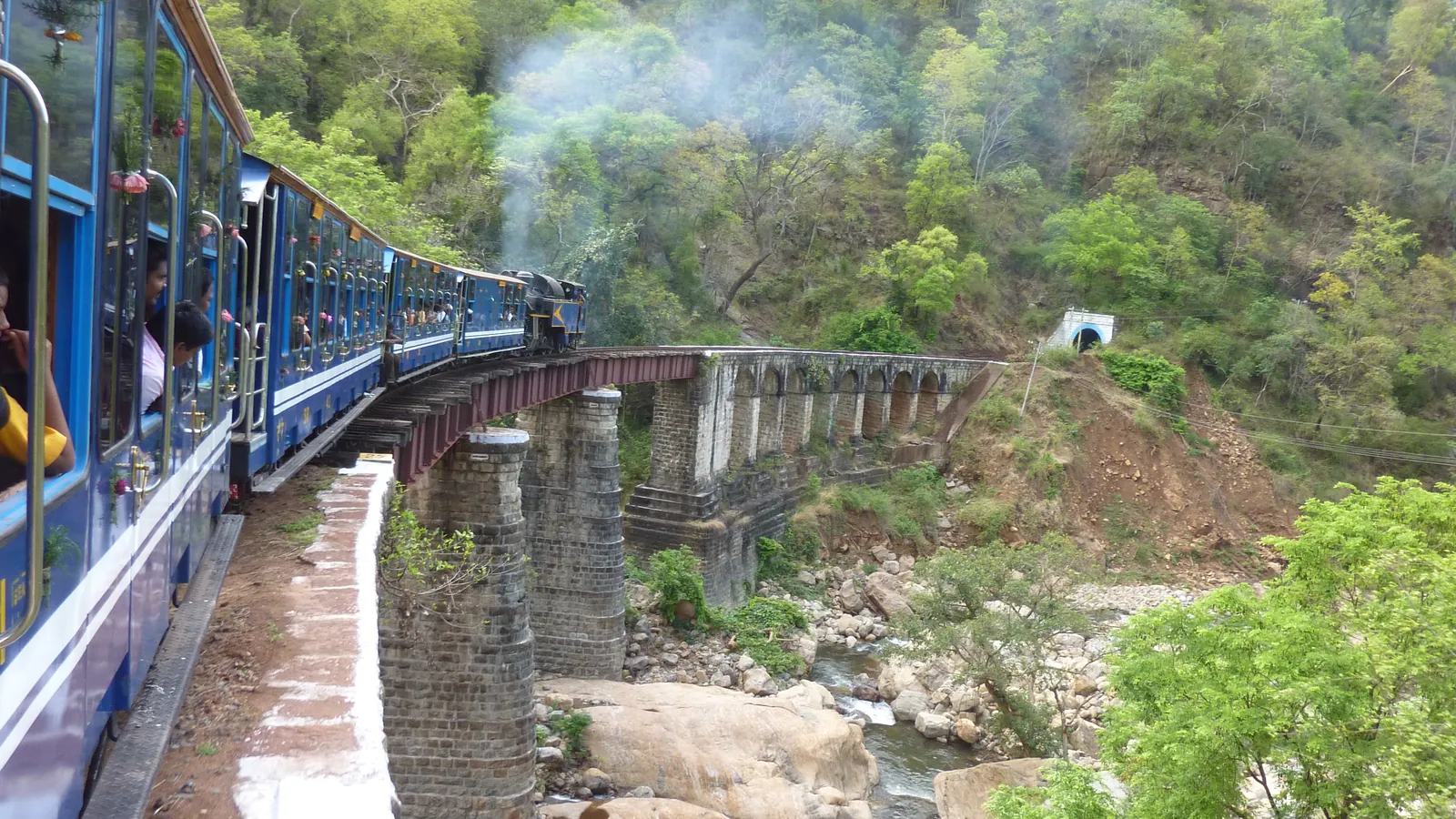 A Nilgiri Mountain Railway train crosses a bridge through the forested Nilgiri hills on its steep climb to Ooty