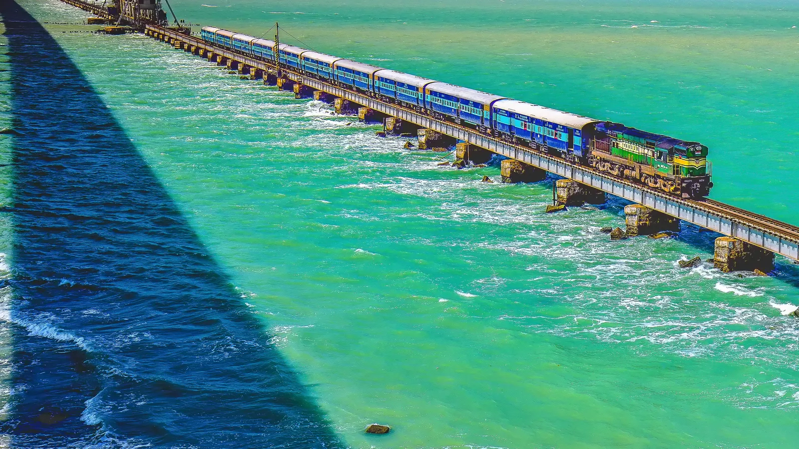 A passenger train crosses turquoise water on the Pamban railway bridge that links mainland India to Rameswaram island