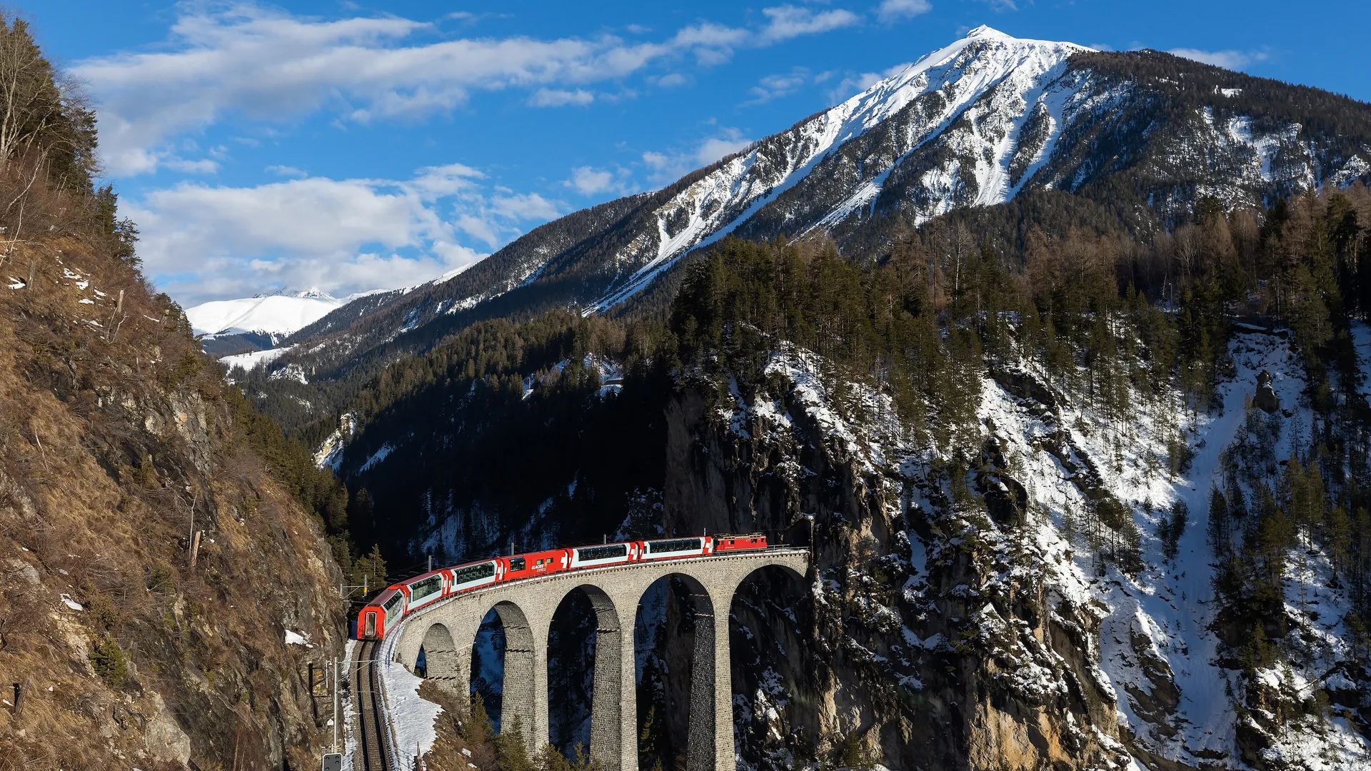 The Glacier Express crosses the curved Landwasser Viaduct in Switzerland, heading straight into a tunnel in the cliff